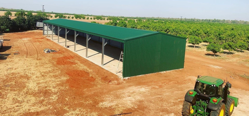 Green steel farm shed beside a John Deere tractor on a dry orchard property